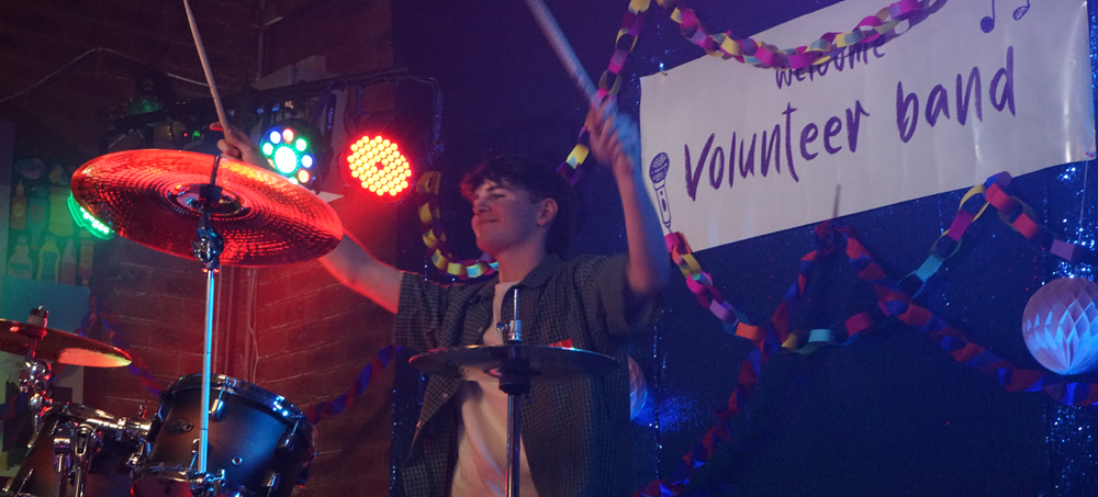 Drummer on stage playing in front of a banner that says volunteer band