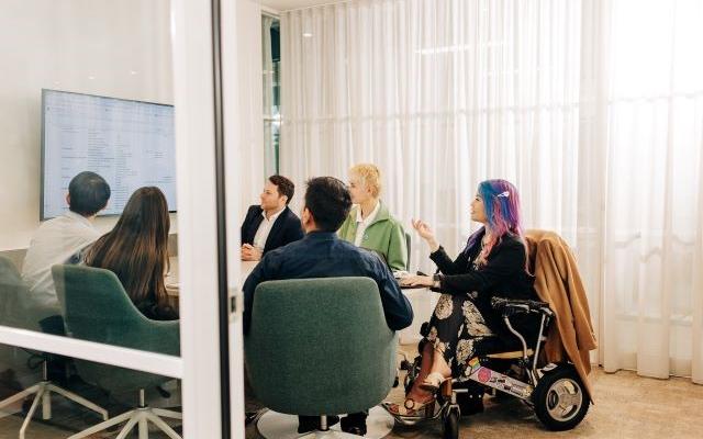 A group of people in a meeting looking at a wall mounted screen.