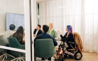 A group of people in a meeting looking at a wall mounted screen.